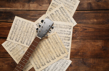 Paper sheets with music notes and guitar neck on wooden table, top view. Space for text