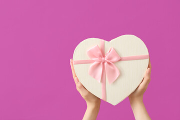 Female hands with gift box in shape of heart on purple background. Valentine's Day celebration