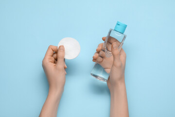 Woman holding makeup remover and cotton pad on light blue background, top view