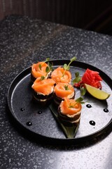 Tasty canapes with salmon, cream cheese and microgreens on dark table