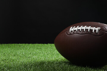 Leather American football ball on green grass against black background, closeup. Space for text