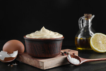 Fresh mayonnaise sauce in bowl and ingredients on black table, closeup