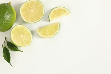 Fresh limes and green leaves on white background, flat lay. Space for text