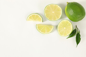 Fresh limes and green leaves on white background, flat lay. Space for text