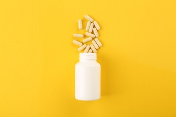 Bottle and vitamin capsules on yellow background, top view