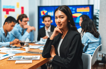 Portrait of happy young asian businesswoman or analyst looking at camera with her colleague analyzing data analysis in dynamic business strategy investment planning meeting. Habiliment