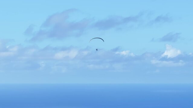 Extreme paraglider flying against a clear blue sky with white clouds. Man flies with paraglide high in sky 4K. Up in the air, cinematic aerial drone shot of paraglider above Pacific ocean, Hawaii USA