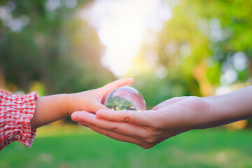Adult person passes crystal ball to baby hand a healthy ecology to a new generation. Healthy ecology of the planet Earth. A healthy future for our generation. green glass background. Save the world.