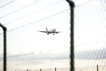 A passenger plane seen from behind a fence approaching to land