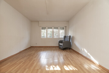 An empty room with a lonely old gray armchair next to a window with bars