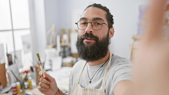 Handsome bearded man painting in a bright art studio, depicting his creativity and passion for fine arts.