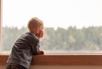 thoughtful alone child at home looking out his window  - Powered by Adobe