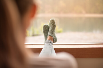 Young woman relaxing at home  feet up early morning looking out her window 