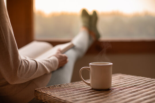 Person relaxing at home reading book feeling relaxed on a cozy winter morning enjoying cup of hot  tea coffee 