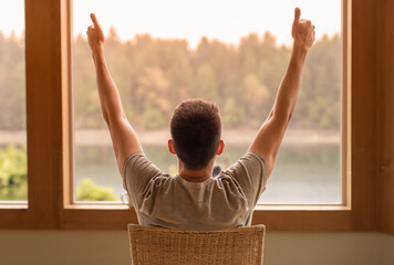 Young man looking out window early morning feeling joyful and positive 