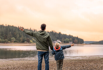 Father and son feeling free together outdoors raising arms up in beautiful nature sunset setting 