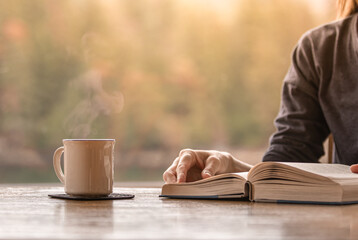Person reading book and enjoying a cup of coffee early morning 