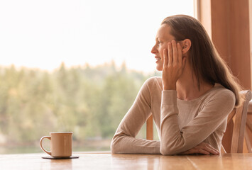 Young woman relaxing looking out window early morning  at the beautiful nature view, enjoying coffee and quiet time. 