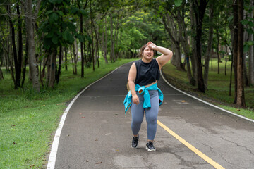 Overweight young woman wiping off her sweat with her left hand on her morning exercise run at...
