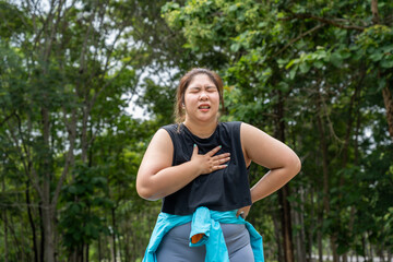Overweight young woman with chest pain putting her right hand over her pain chest during her...