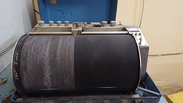 Seismograph records an earthquake on the sheet of measuring paper. Seismological device for measuring earthquakes. Earthquake wave on graph paper. Human finger showing a detail of the earthquake.