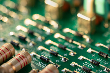 An electronic circuit board made of green fiberglass with many soldered ceramic-painted resistors and capacitors on conductor tracks with color-coded numbers and letters. Computer circuit close-up.