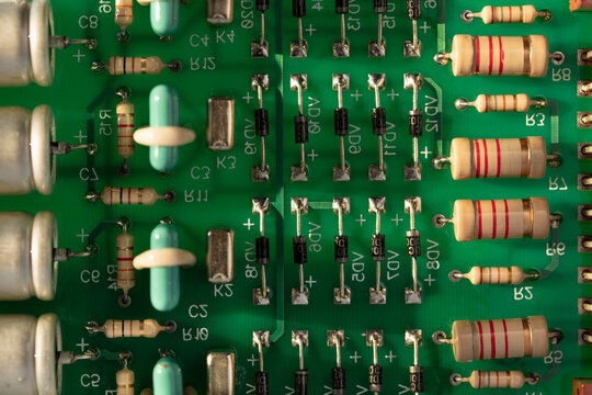 An electronic circuit board made of green fiberglass with many soldered ceramic-painted resistors and capacitors on conductor tracks with color-coded numbers and letters. Computer circuit close-up.
