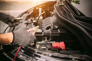 Close-up hand auto mechanic using connect jumper cables on terminal dead battery for jump-start or...