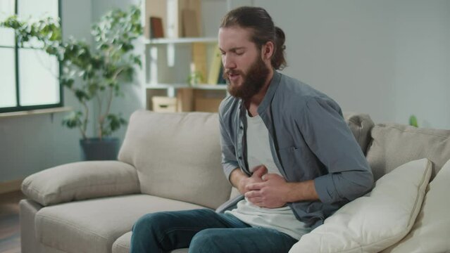 Man sitting on the couch suddenly felt pain in his stomach. Man trying to relieve pain by massaging his stomach