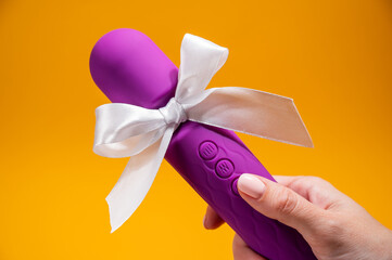Woman holding purple vibrator with white bow on orange background. 