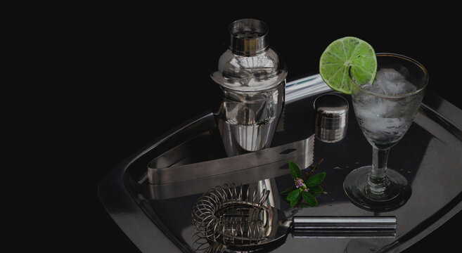 Kit de coctelería. Cóctel refrescante con rodaja de limón y menta. Coctelera, colador, pinzas de hielo y bandeja de acero inoxidable. Taller o curso de coctelería. Fondo negro y espacio para copiar. 