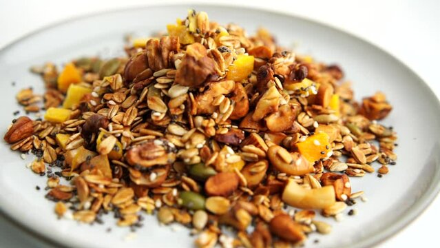 Healthy organic granola breakfast flakes with almonds, cashew nuts walnuts, hazelnuts, pumpkin seeds and cranberries circle rotation close up top view.
