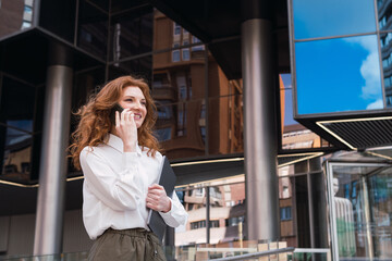 Caucasian business woman leaving office with laptop while talking with phone