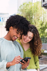 Two female college classmates looking at phone of one of them and laughing as they walk across campus.