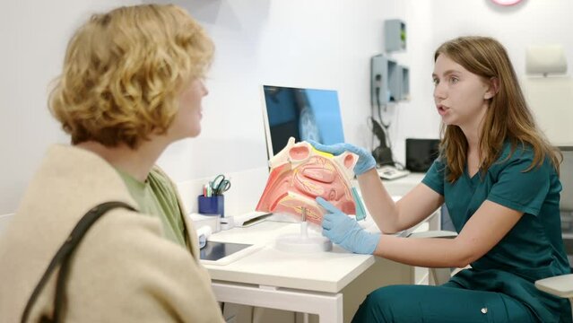 A otolaryngologist doctor explains to a patient about his illness at an appointment. Professional ENT doctor shows the features of a nose and sinus disease. Sinusitis, nasal septum deviation problems