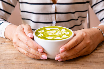 A woman holds a cup of matcha green tea with milk cream. She is about to drink green tea in the morning. Welcome the freshness of the new day.