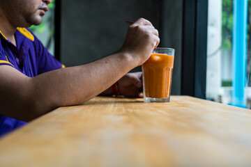 Man drinks delicious Thai milk tea while sitting at a table in a cafe enjoying free time.