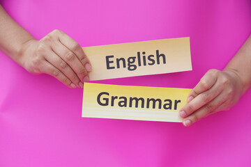 Close up hands hold  word card paper with text English grammar. Pink background. Concept, English language grammar teaching. Using word card to create for playing educational fun games or practice