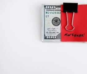 A red paper note clipping on dollars bank notes with handwritten text MORTGAGE, concept of saving or set budget for house loan or mortgage payment - on white background can used as copy space