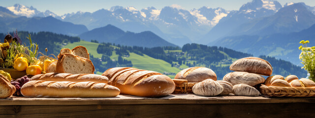 Assortment of fresh bread on a wooden table with the picturesque snow peaks mountains in the background, evoking the essence of artisanal baking. - obrazy, fototapety, plakaty
