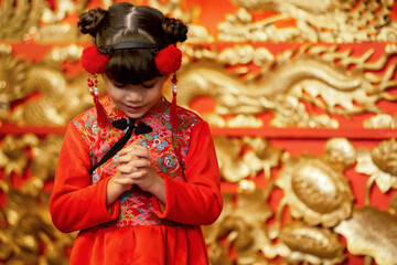 Cute little girl wearing a red Chinese traditional dress is doing a Chinese hello or thank you gesture during Chinese New Year