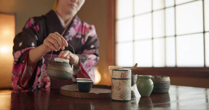 Traditional Japanese woman, pot and tea cup for health, wellness or liquid to relax at tearoom table. Girl, person and hands with drink for culture, detox and indigenous clothes with peace in home