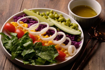 fresh vegetable salad, edamame, sweetcorn, cherry tomatoes, romaine lettuce, sliced cucumber, sliced onions, and purple cabbage. extra virgin olive oil. served on a white ceramic plate. appetizer. 