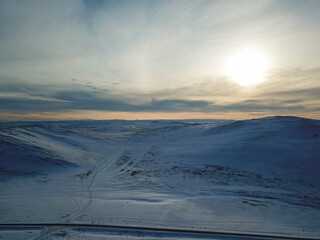 A bird's eye view of a ridgeline half-covered with snow in a forest with a sunburst in the upper...