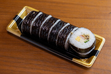 プラスチック容器に入ったお惣菜の太巻き寿司 © decoplus