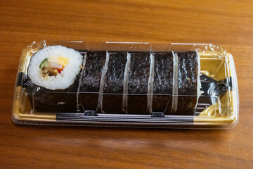 透明な蓋をしたプラスチック容器に入ったお惣菜の太巻き寿司