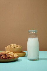 Minimal scene of a glass bottle filled with soya milk, decorated with wooden dishes of soybeans and nuts. Soybean contains proteins and active phytohormones