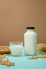 Soya milk filled inside a cup and unbranded bottle, displayed with a lot of soybeans over beige background. Soybeans are rich in water-soluble vitamins