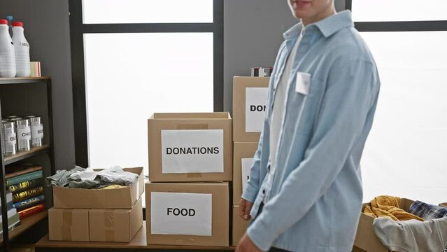 Young, confident, and smiling, a caucasian man volunteer points to himself at the charity center. surrounded by donation boxes, his altruistic spirit stands out bright in the warehouse.