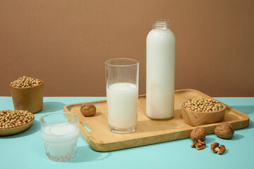 Blank label bottle and a glass filled with organic milk displayed on wooden tray. Few walnuts featured. Soybeans are a breakfast special for many cultures